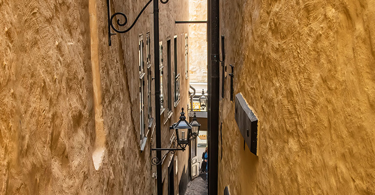 Wąska, brukowana uliczka w Gamla Stan, Sztokholm, z zabytkowymi żółtymi budynkami i latarniami ulicznymi.