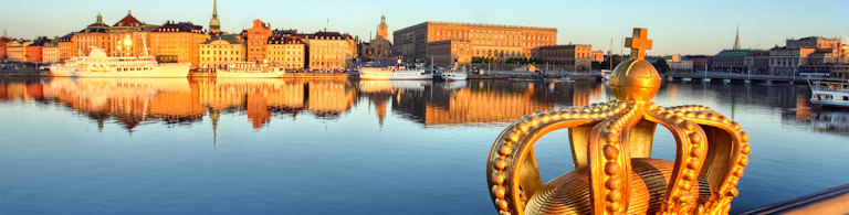 Szersza panorama Sztokholmu o wschodzie słońca z Gamla Stan i Pałacem Królewskim, z dekoracyjną złotą koroną na moście na pierwszym planie