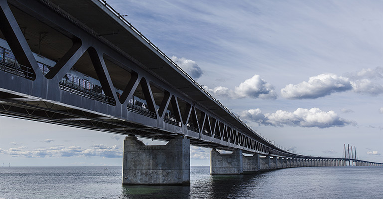 Rozległy most Øresund rozciąga się nad wodami cieśniny, łącząc lądy pod błękitnym niebem z chmurami.