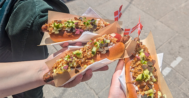 Duńskie hot dogi (pølser) trzymane w rękach z małymi duńskimi flagami. Street food w Kopenhadze.