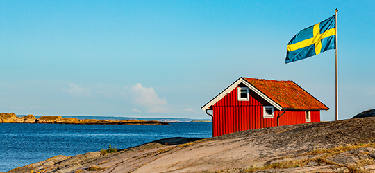 Rotes Schwedenhaus mit Schwedenflagge am Meer