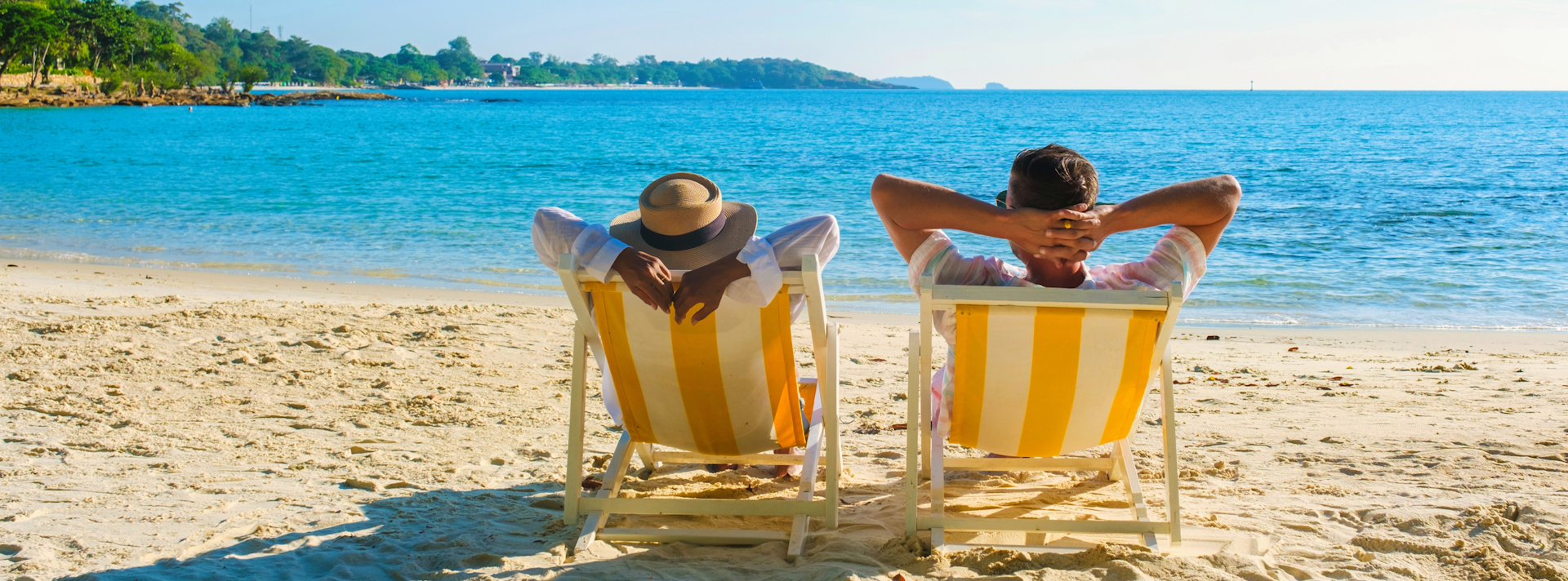 Ett par som sitter i solstolar på en strand och tittar ut över havet