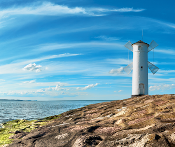 Vit fyr i form av väderkvarn vid havet i Świnoujście under blå himmel.