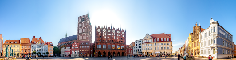 Soligt torg i Stralsund med färgglada hus och gotiskt rådhus.
