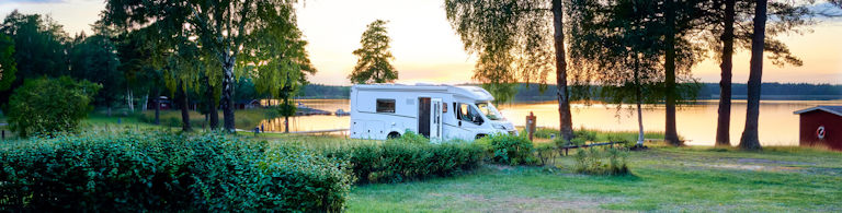 Husbil parkerad vid en sjö i solnedgången. Campingsemester i Europa